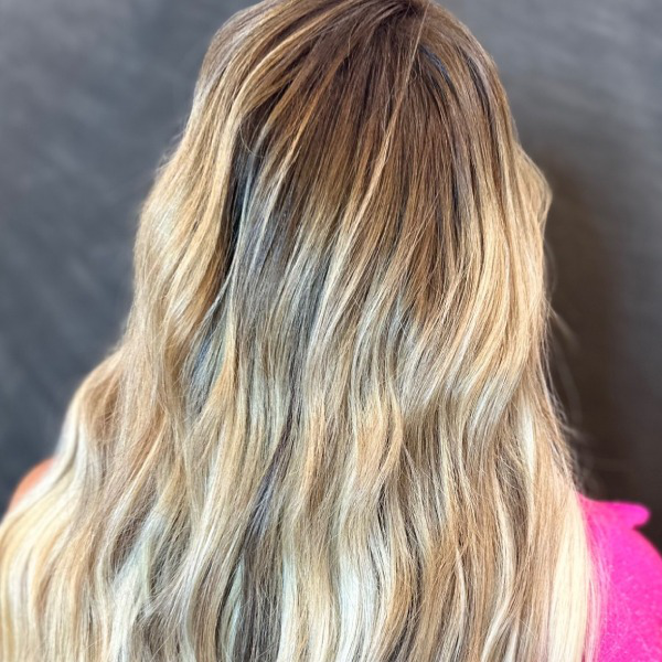 A close-up of a woman’s hair showing a smooth root blending transition from rich brown roots to soft blonde ends